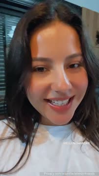 Morena de cabelo liso sorri pro celular com tímida sensualidade